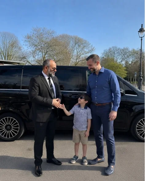 Chauffeur greeting a father and child beside a black Mercedes van in a Paris park setting